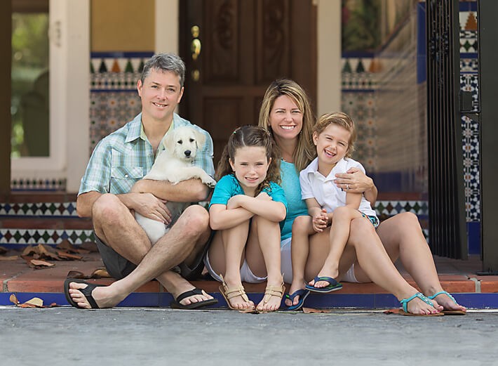 Family photo with new puppy in front of Mediterranean style home