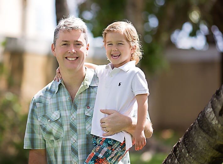 Son and dad posing for a shot together outside in the sun