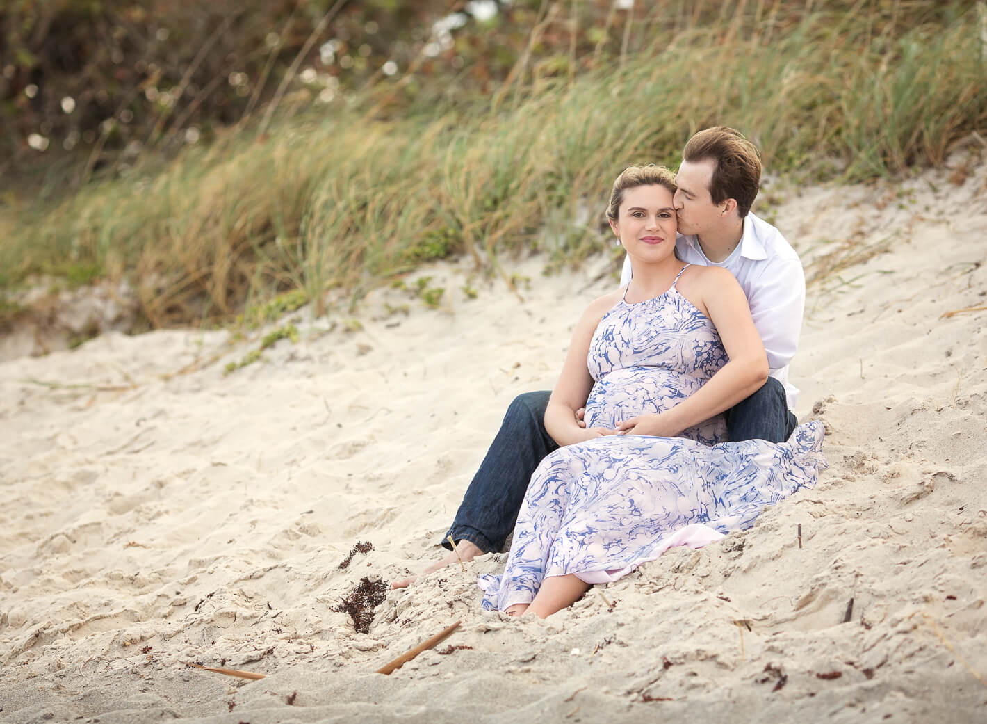 Dad kissing mom-to-be on beach during maternity session