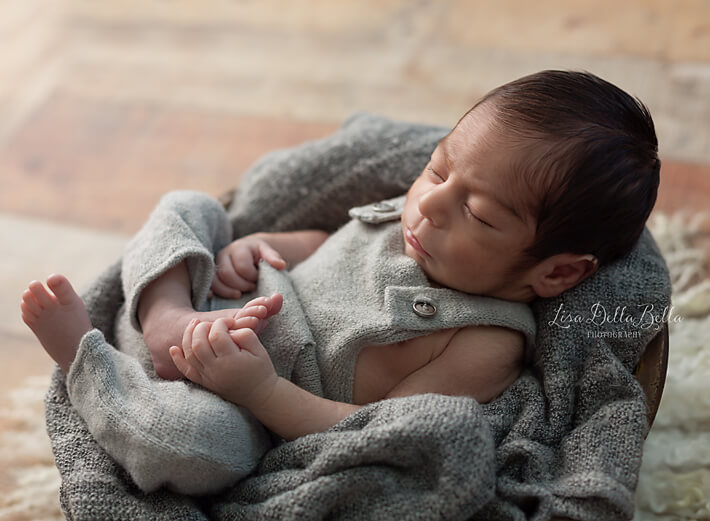 Newborn boy in bowl holding his foot