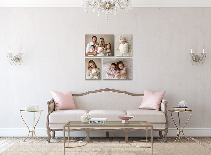 A chic living room features a beige sofa adorned with pink cushions, surrounded by modern side tables and delicate chandeliers. The pale walls display three family portraits: a couple with their baby, a newborn, and three children together. This space is an investment in warmth and family memories.